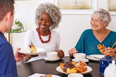 Two women enjoy tea and cake with a carer