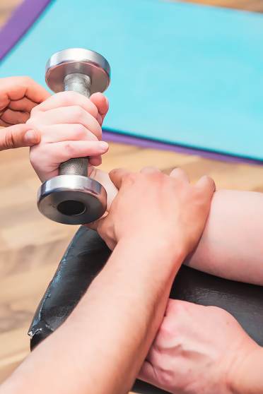 Close up of an arm lifting a hand weight, guided by other pair of hands
